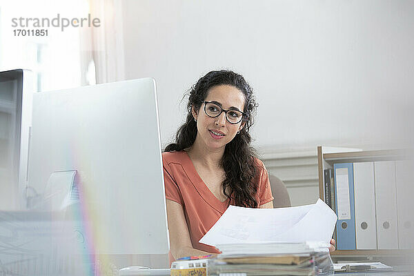 Weibliche Fachkraft  die ein Papierdokument hält und auf einen Computer im Büro schaut