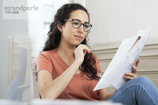Weibliche Fachkraft liest ein Dokument  während sie im Büro sitzt