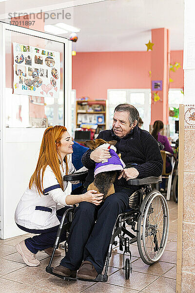 Behinderter Mann und Krankenschwester mit Haustier im Pflegeheim