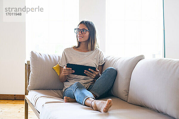 Nachdenkliche brünette Geschäftsfrau sitzt mit digitalem Tablet auf dem Sofa im Wohnzimmer zu Hause