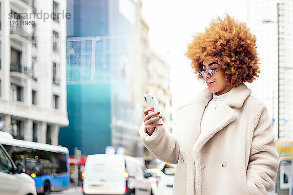 Frau mit afroblondem Haar  die ein Smartphone benutzt  während sie auf der Straße steht