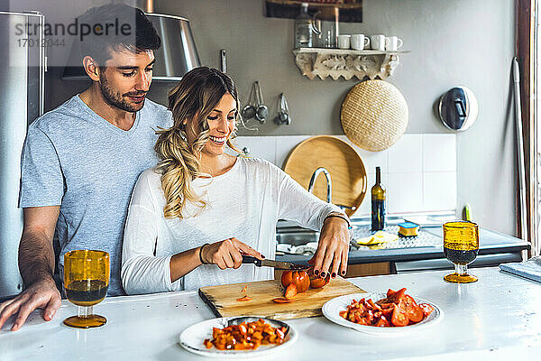 Junge Frau hackt Tomaten  während sie Abendessen kocht und ein Mann zusieht