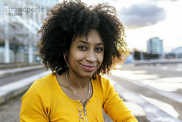 Nahaufnahme einer lächelnden Frau mit Afro-Haar  die über Kopfhörer Musik hört  gegen den Himmel