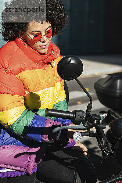 Weibliche Bikerin mit bunter Jacke auf dem Motorrad sitzend an einem sonnigen Tag