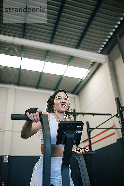 Lächelnde Sportlerin bei der Arbeit an einem Trainingsgerät im Fitnessstudio