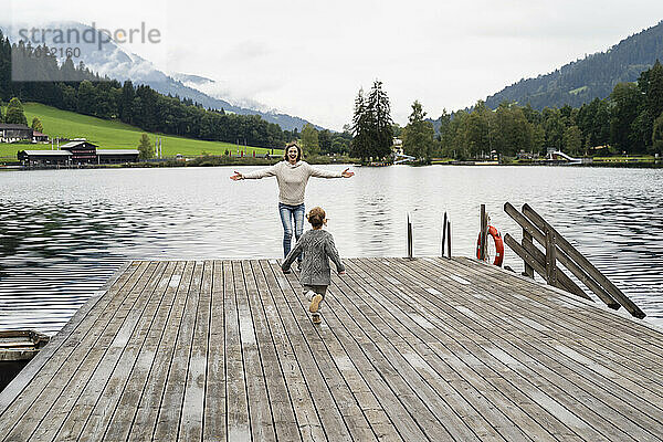 Kleines Mädchen rennt auf die Mutter zu  die mit offenen Armen am Rande des Seeuferstegs steht