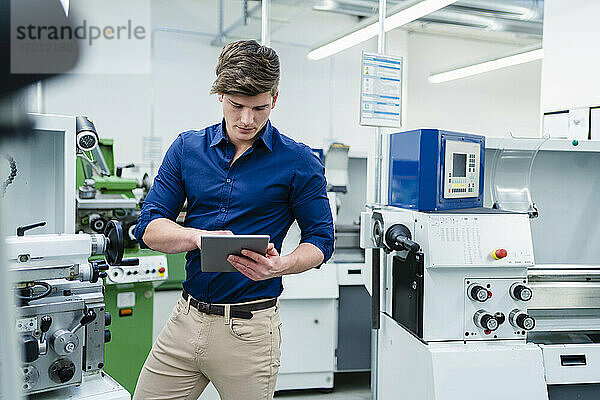 Männlicher Fachmann  der ein digitales Tablet an einer Produktionsanlage in einer Fabrik benutzt