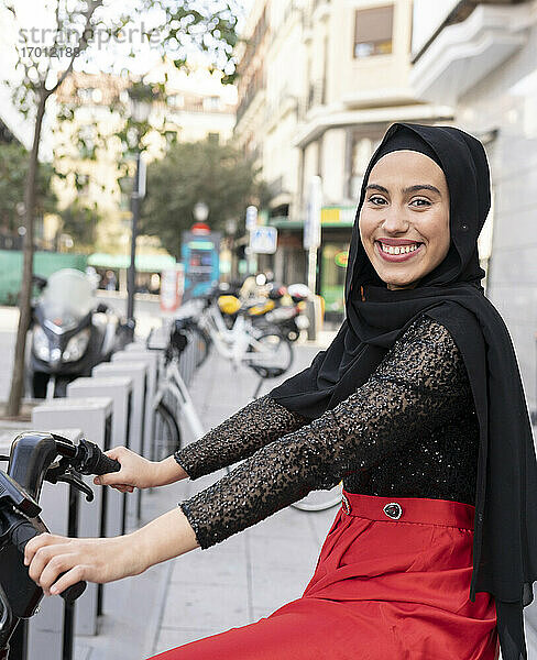 Porträt einer jungen Frau mit Hidschab  die auf einem Mietfahrrad sitzt