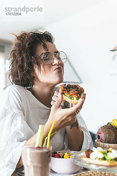 Porträt einer jungen Frau mit Brille und Nasenring beim Frühstück
