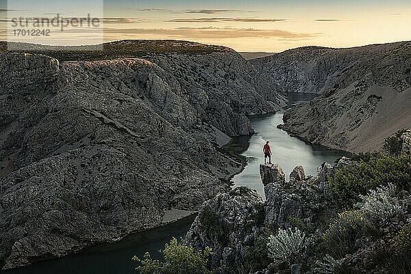 Mann steht auf Felsen und schaut auf den Fluss in einer Schlucht bei Sonnenuntergang