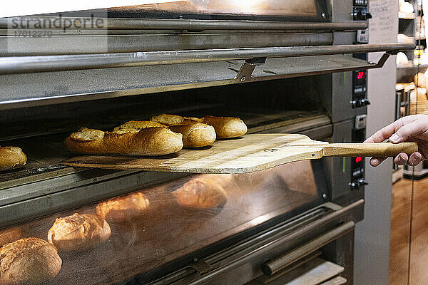 Männlicher Koch nimmt frisch gebackenes Brot mit Pizzaschieber aus dem Ofen in einer Bäckerei