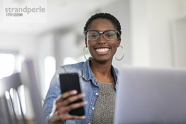 Lächelnde Frau bei der Arbeit mit Laptop und Smartphone zu Hause
