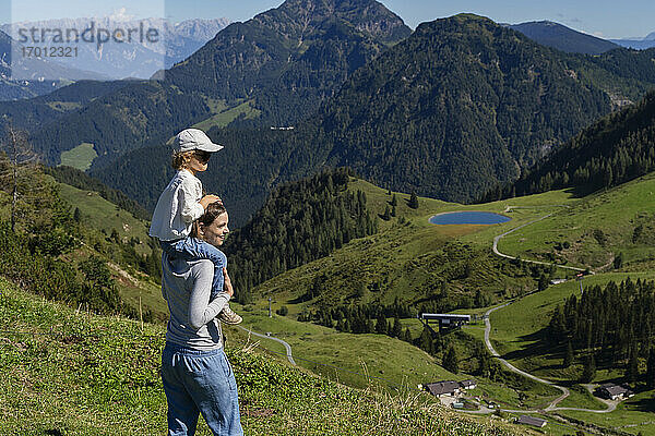 Mutter nimmt ihre kleine Tochter bei einer Wanderung in den frühlingshaften Bergen huckepack