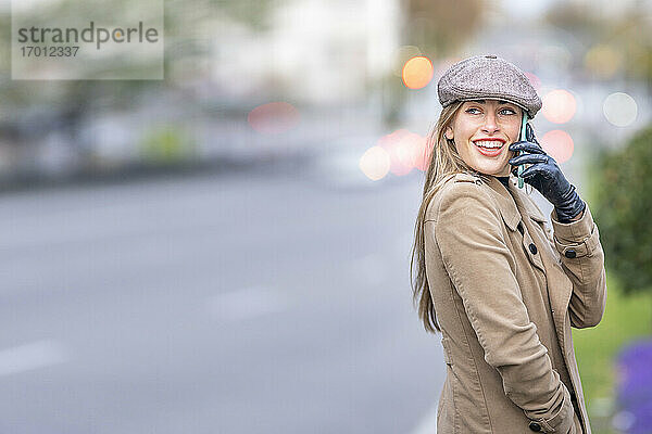 Lächelnde attraktive Frau  die auf der Straße steht und mit einem Smartphone spricht