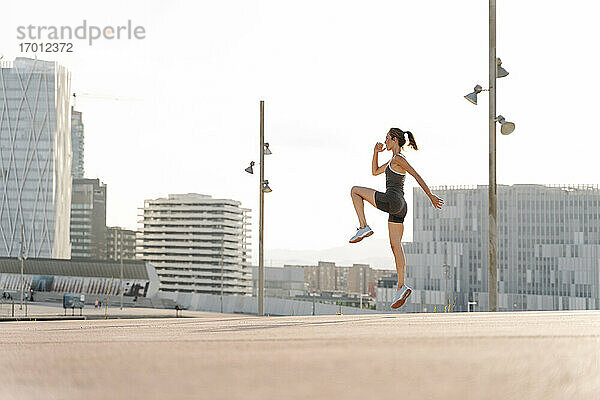 Mittlere erwachsene Sportlerin bei einer Sprungübung an einem sonnigen Tag in der Stadt