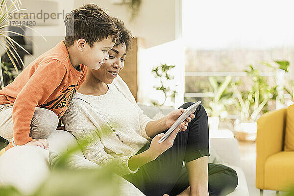Frau zeigt einem Jungen zu Hause sitzend ein digitales Tablet