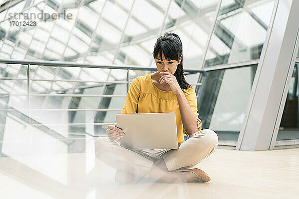 Unternehmerin arbeitet an einem Laptop  während sie im Flur eines Büros sitzt