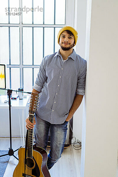 Lächelnder Gitarrist mit gestricktem Haar  stehend mit Gitarre im Studio