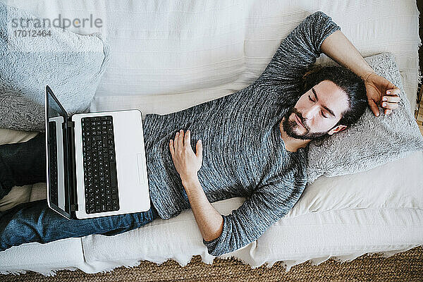 Mann mit Laptop schlafend auf Sofa zu Hause