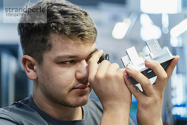 Junger Ingenieur bei der Untersuchung eines kleinen Mikroskops während der Arbeit in der Industrie