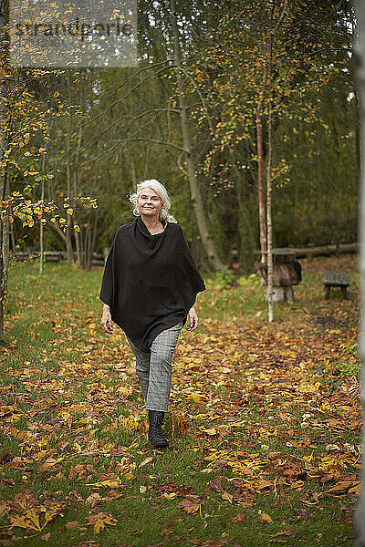 Selbstbewusste ältere Frau  die im Herbst im Park über das Gras läuft