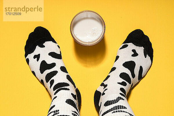 Mann Fuß mit Kuhdruck Socken und Glas Milch auf gelbem Hintergrund im Studio