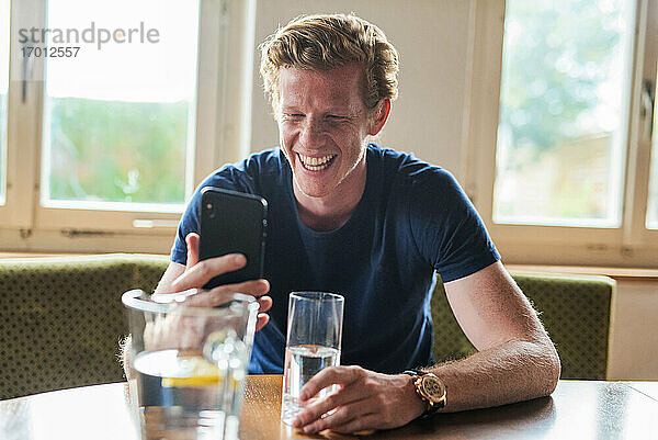 Mann lacht während eines Videoanrufs über sein Smartphone im Wohnzimmer