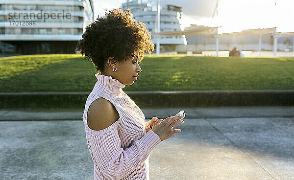 Frau mit Afro-Haar  die ein Mobiltelefon benutzt  während sie auf der Straße in der Stadt steht