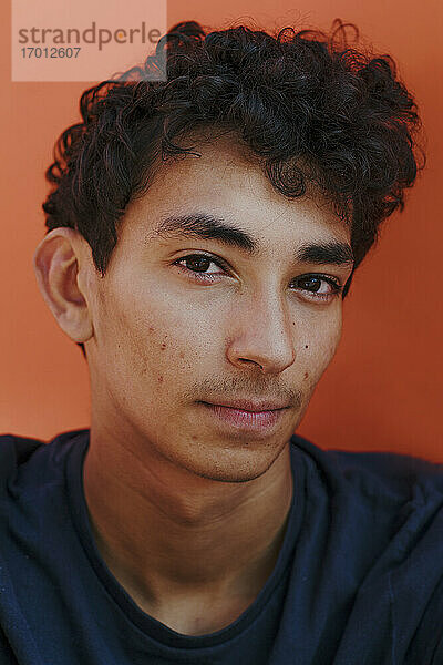 Nahaufnahme eines gut aussehenden jungen Mannes mit lockigem Haar vor einer orangefarbenen Wand