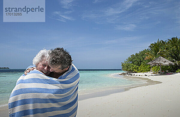 Indischer Ozean  Malediven  Ari Atoll  Vilamendhoo Insel  Glückliches Paar in gestreiften Strandtuch auf tropischen Strand gewickelt