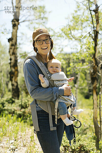 USA  Utah  Uinta National Park  Porträt einer lächelnden Frau mit Baby-Sohn (6-11 Monate) in Babytrage im Wald