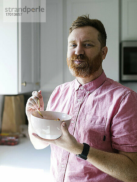 Porträt eines Mannes  der in der Küche Müsli frühstückt