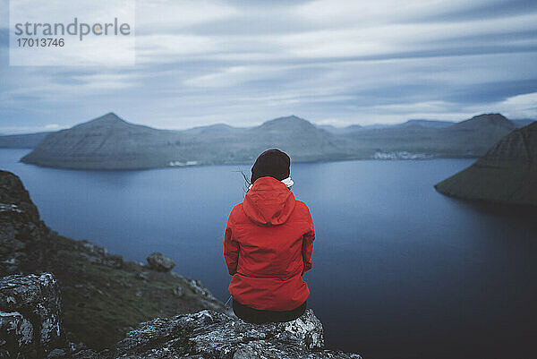 Dänemark  Färöer Inseln  Klaksvik  Frau sitzt am Rande einer Klippe über dem Meer und schaut auf die Aussicht