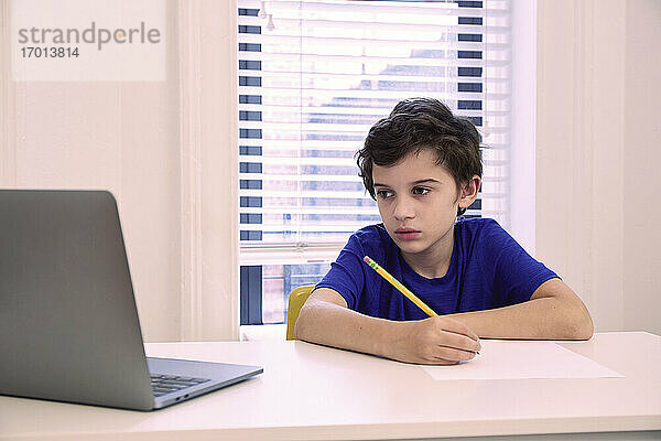 Junge (8-9) sitzt zu Hause am Schreibtisch während des Fernunterrichts