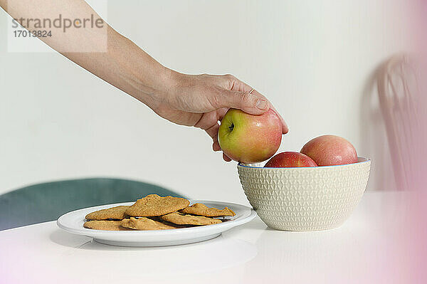 Nahaufnahme einer Frauenhand  die einen Apfel aus einer Schale nimmt