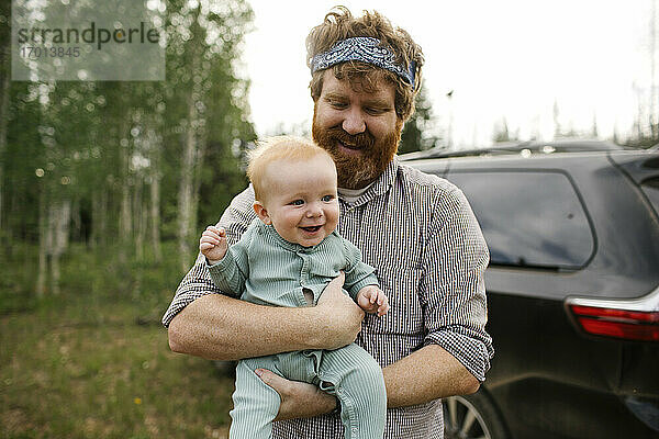 USA  Utah  Uinta National Park  Lächelnder Mann hält Baby-Sohn (6-11 Monate) im Feld  Auto im Hintergrund