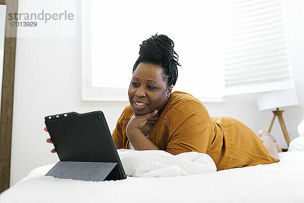 Lächelnde Frau auf dem Bett liegend und mit Tablet