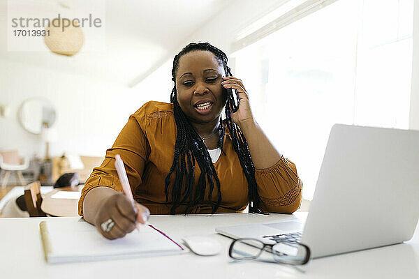 Frau arbeitet zu Hause am Schreibtisch  schreibt und spricht mit dem Handy