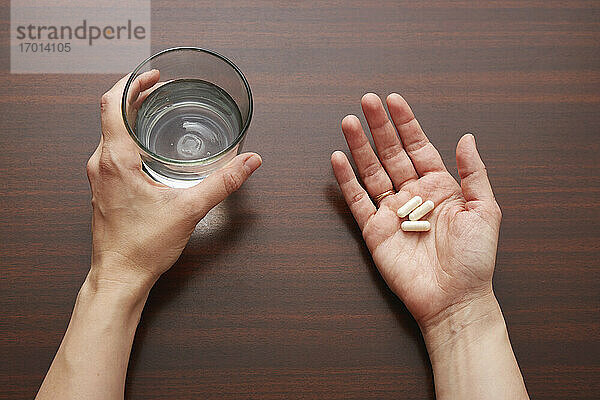 Frauenhände halten Pillen und Glas Wasser