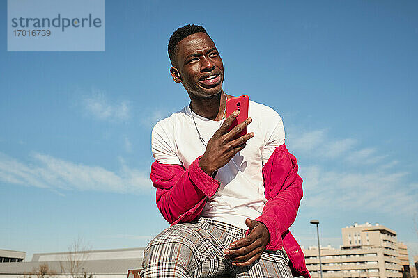 Junger Mann in roter Jacke schaut im Freien auf sein Smartphone