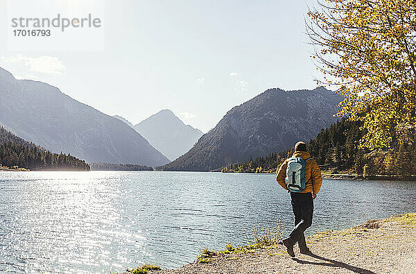 Männlicher Wanderer mit Rucksack am See gegen den Himmel an einem sonnigen Tag