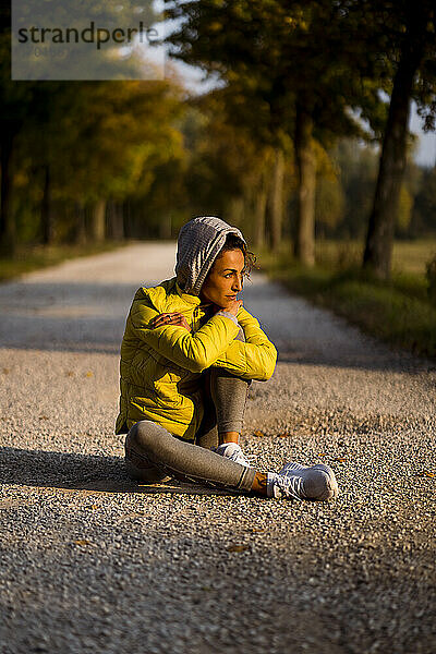 Sportlerin mit Kapuzenshirt schaut weg  während sie auf der Straße sitzt