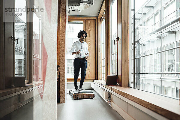 Aktiver männlicher Unternehmer  der auf einem Laufband läuft und dabei auf einen Laptop am Fenster im Büro schaut