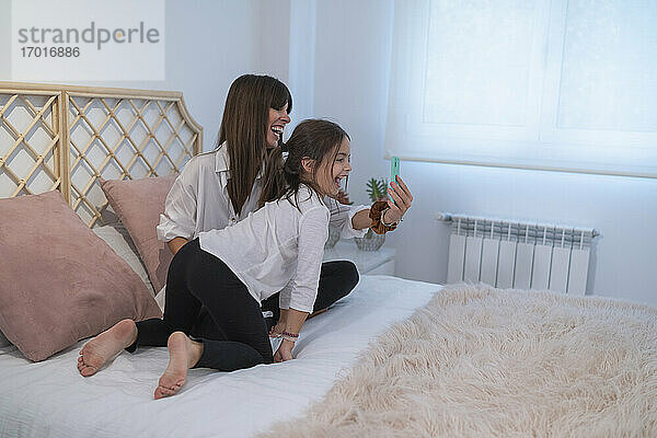 Glückliche Mutter und Tochter bei einem Videogespräch mit dem Vater über ein Smartphone im Schlafzimmer