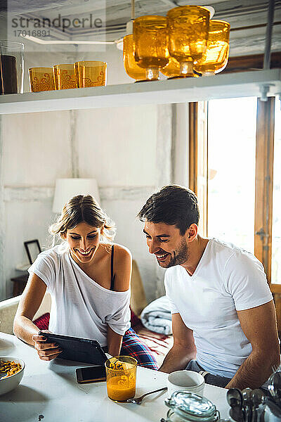 Glückliches junges Paar  das beim Frühstück zu Hause ein Tablet betrachtet