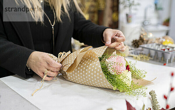 Florist wickelt Blumenstrauß mit Papier im Blumenladen ein