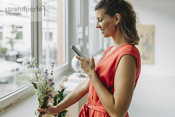 Lächelnde Frau fotografiert Blumen mit Smartphone