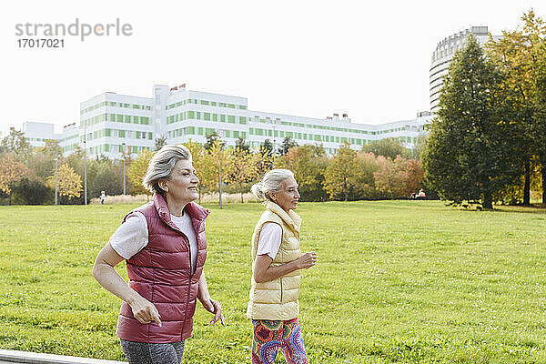 Lächelnde Freundinnen laufen im öffentlichen Park an einem sonnigen Tag