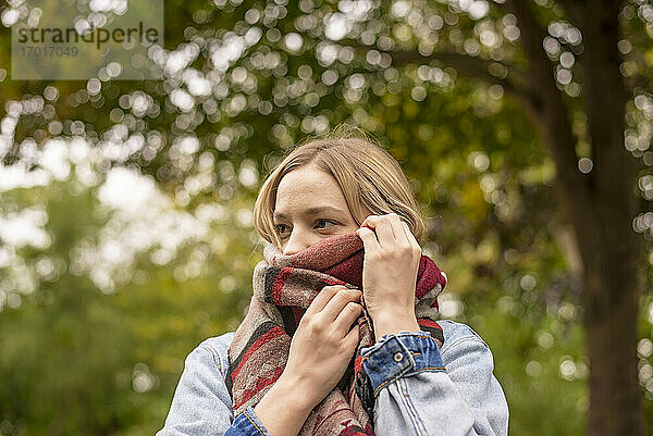 Junge Frau bedeckt Gesicht mit Schal im Park