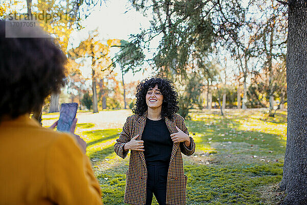 Frau fotografiert lächelnden Freund mit dem Handy  während sie im Park steht